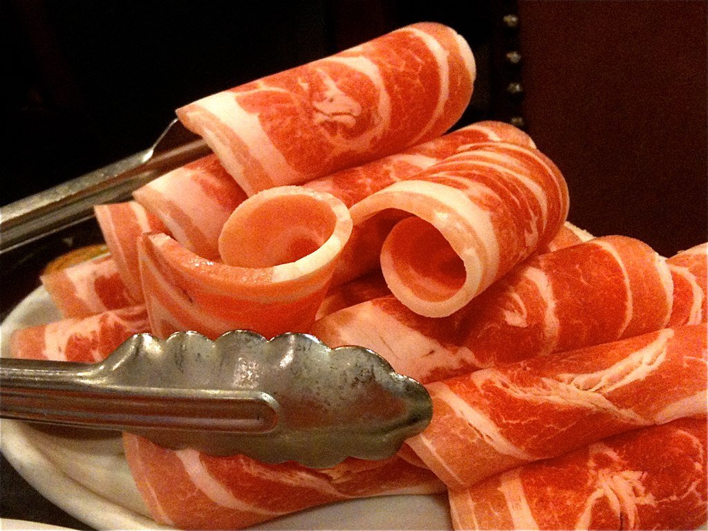 Thin-sliced daepae-samgyeopsal pork belly draped over a grill
