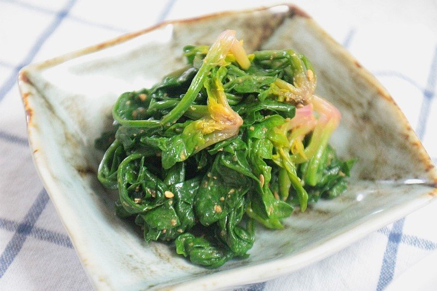 A square white dish of dark green seasoned spinach namul with visible sesame seeds
