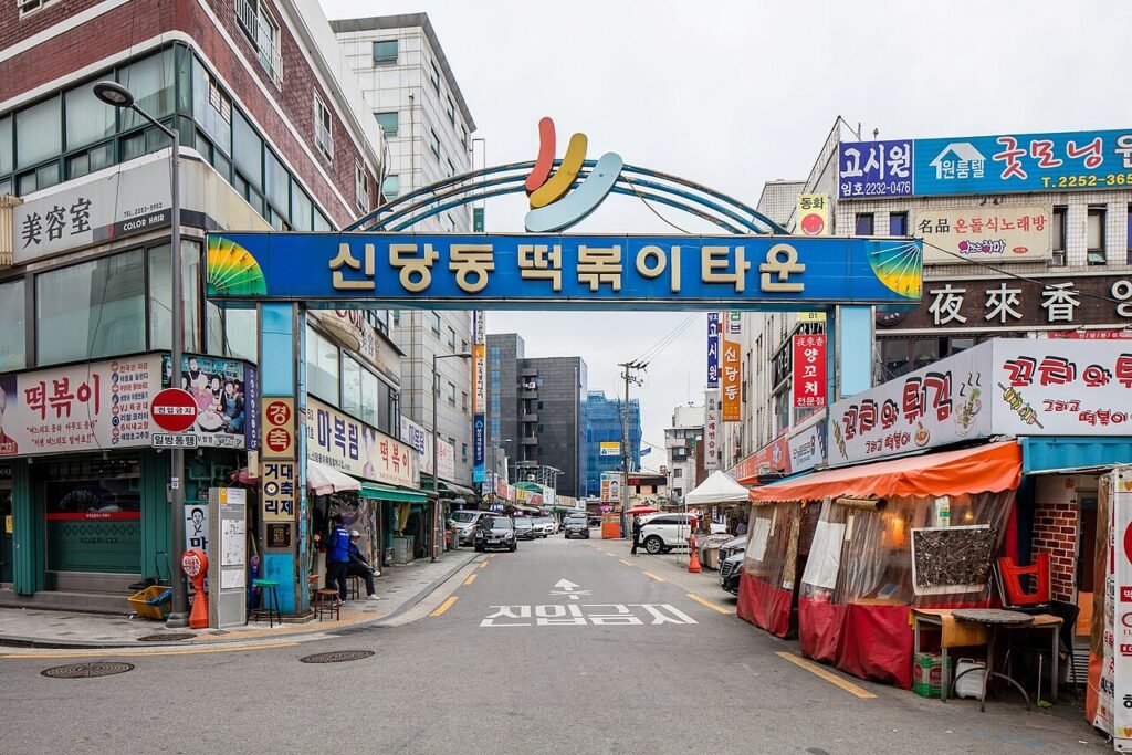 A blue arch sign reading Sindang-dong Tteokbokki Town over a street lined with red-signed restaurants