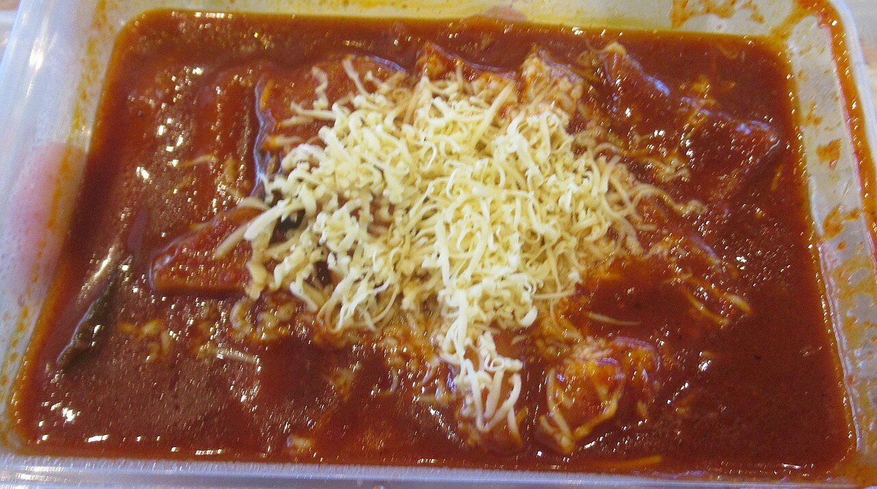 Tteokbokki topped with a layer of melted cheese pulled up in a long string