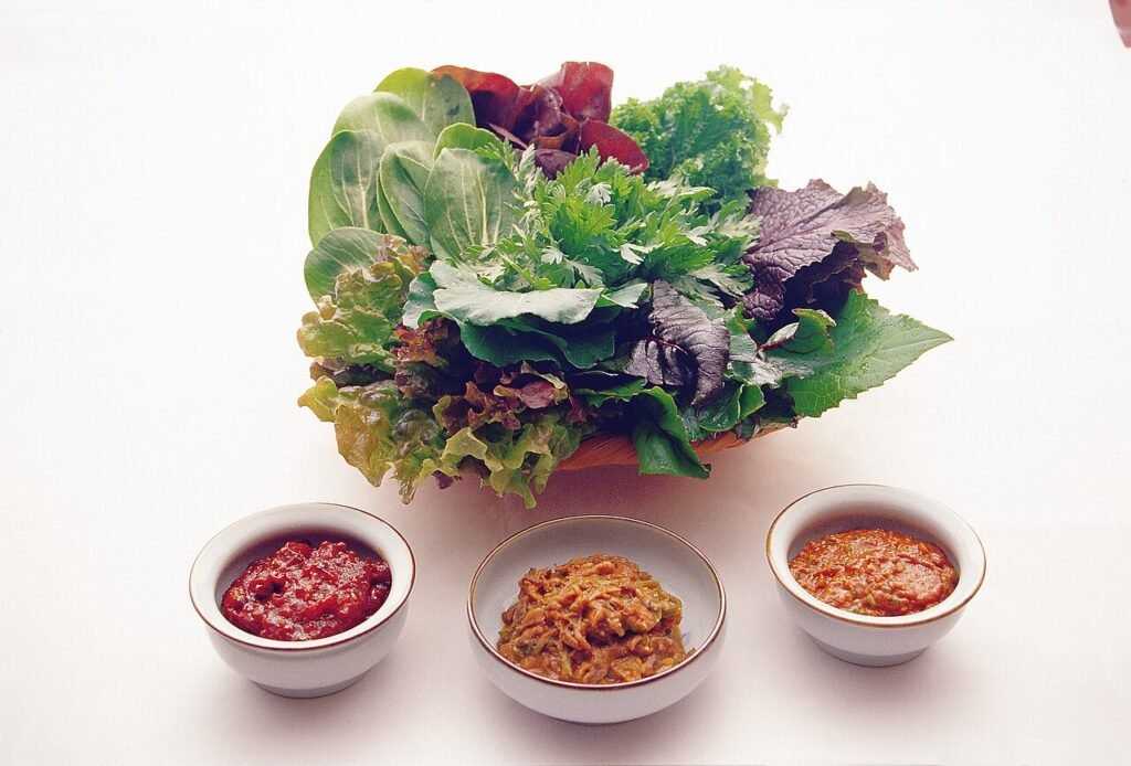 A small bowl of ssamjang next to fresh lettuce and perilla leaves for wrapping grilled meat