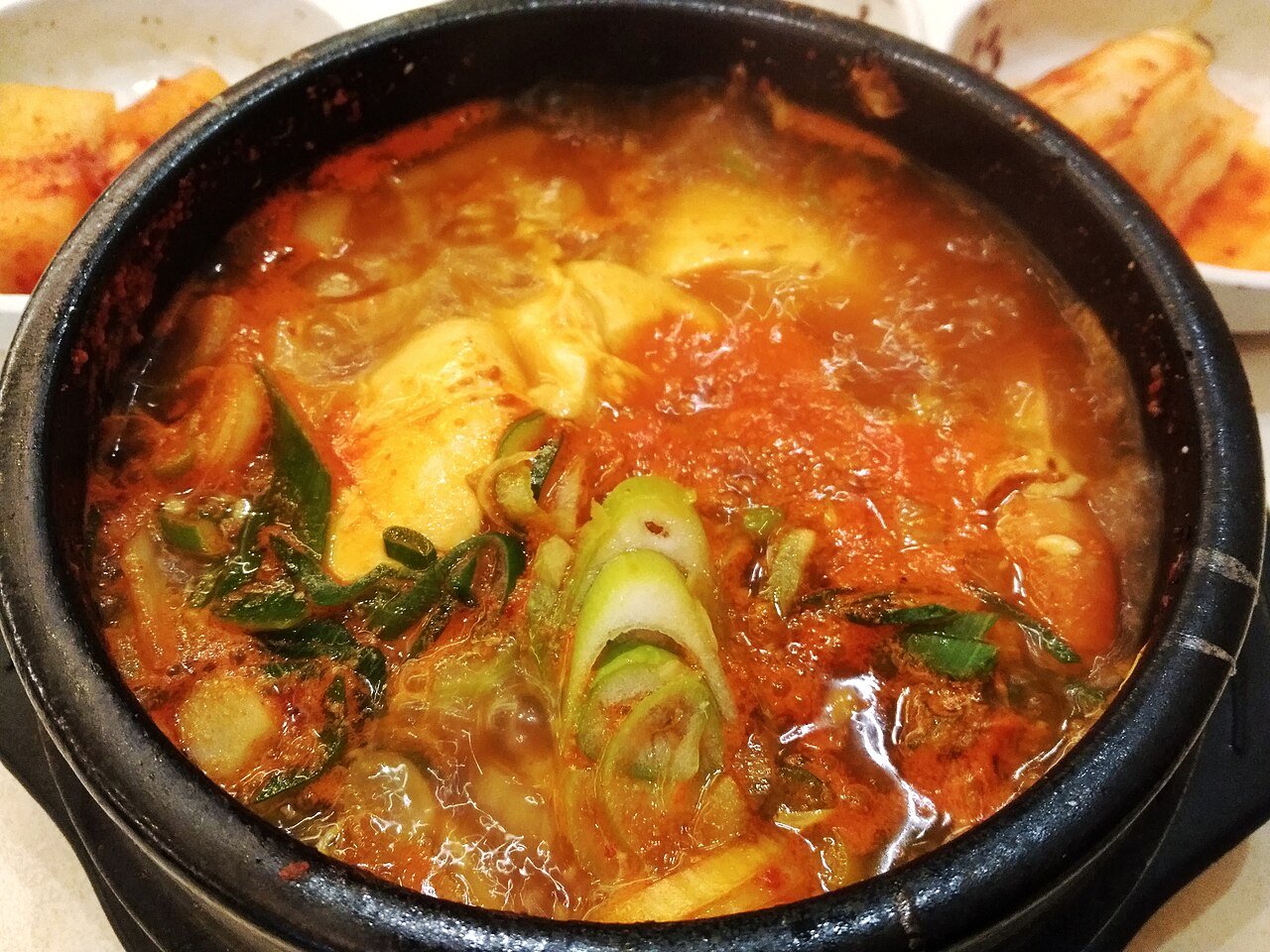 A bubbling earthenware pot of red seafood sundubu jjigae with soft tofu curds and scallions