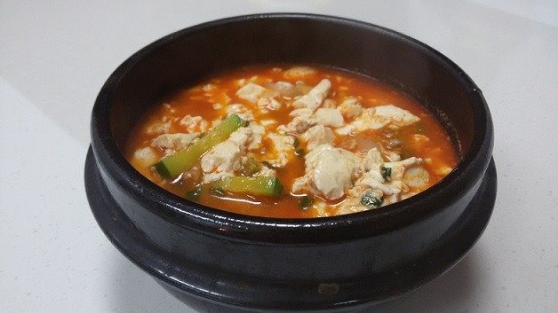 Sundubu jjigae served in a black stone bowl with a side of rice