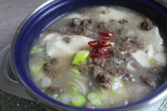 Beef sundubu jjigae in a shallow pot, red broth with visible tofu and sliced scallion