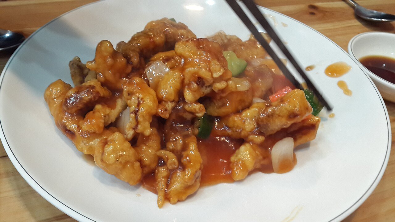 A platter of Korean tangsuyuk, fried pork strips coated in glossy sweet and sour sauce with carrot and onion