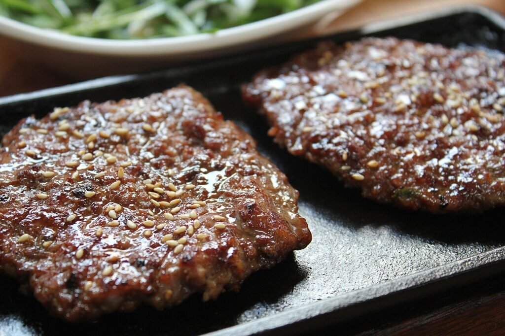 Grilled tteok-galbi patties with a glossy caramelized surface, plated with lettuce and rice