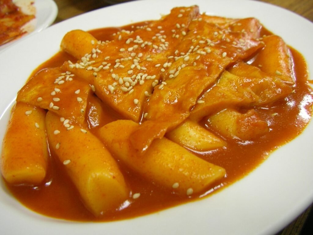 A pan of tteokbokki, cylindrical white rice cakes coated in thick red gochujang sauce with sliced fish cake
