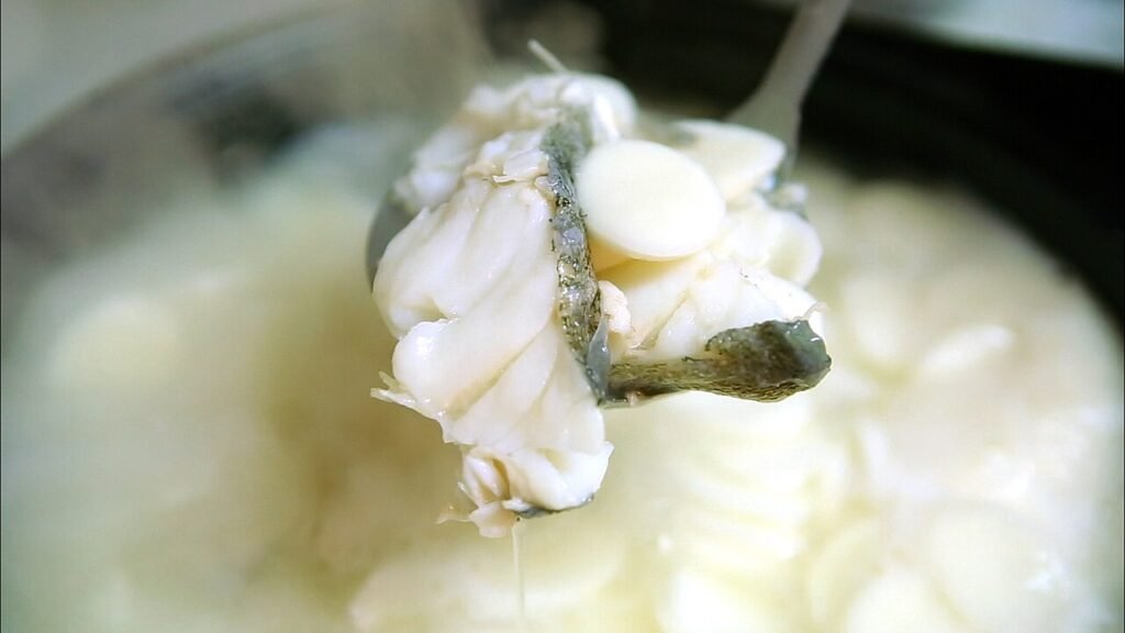 A bowl of tteokguk with sliced white rice cake, beef, egg garnish strips and seaweed in a clear broth
