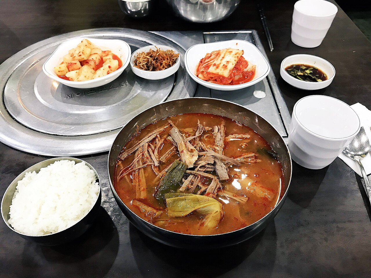 Yukgaejang served in a black stone bowl, red broth with visible scallion and shredded beef