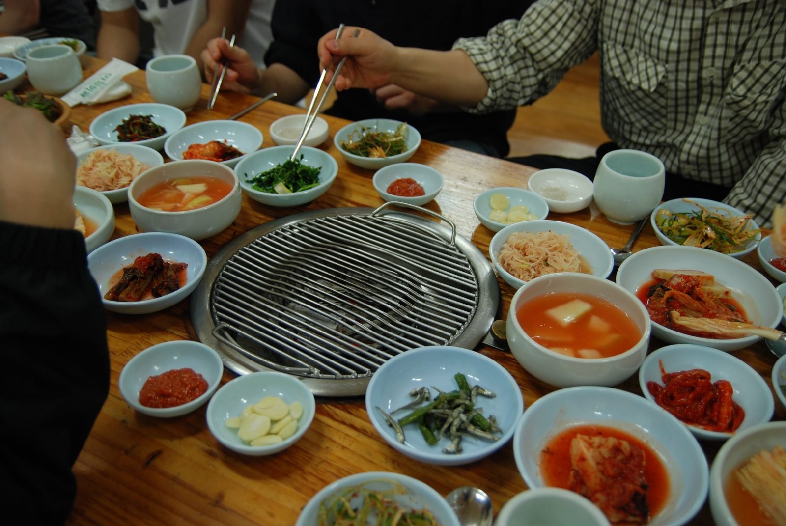 Diners seated around a table with a metal grill in the centre and many small bowls of side dishes