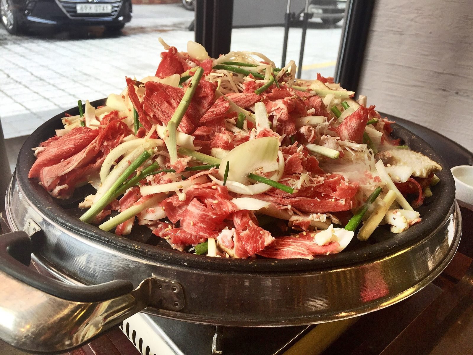 Large pan piled with sliced raw marinated beef, onion and scallions at a Korean restaurant