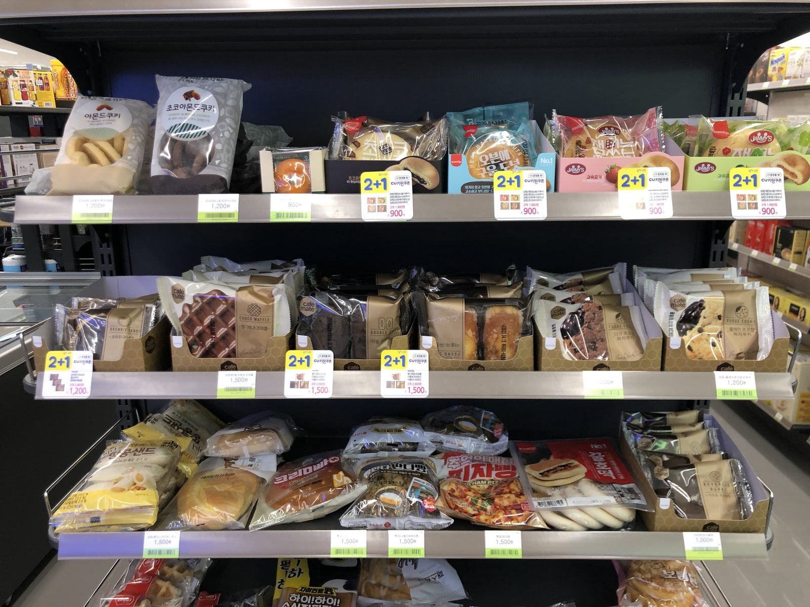Three shelves of packaged cookies, waffles and soft breads with yellow price tags in a CU convenience store