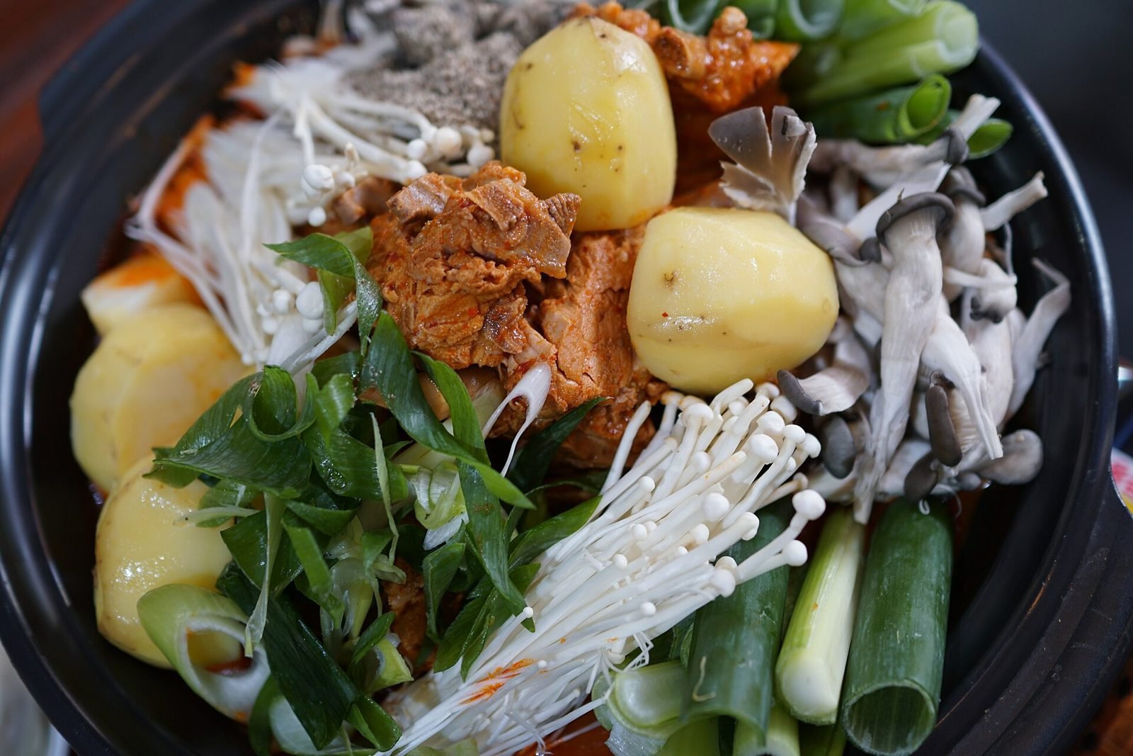 Pork bone stew pot topped with potatoes, enoki mushrooms and scallions