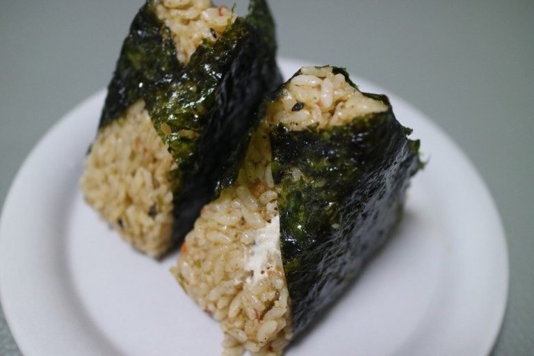 Two triangle kimbap pieces with seaweed wrapped around rice on a white plate