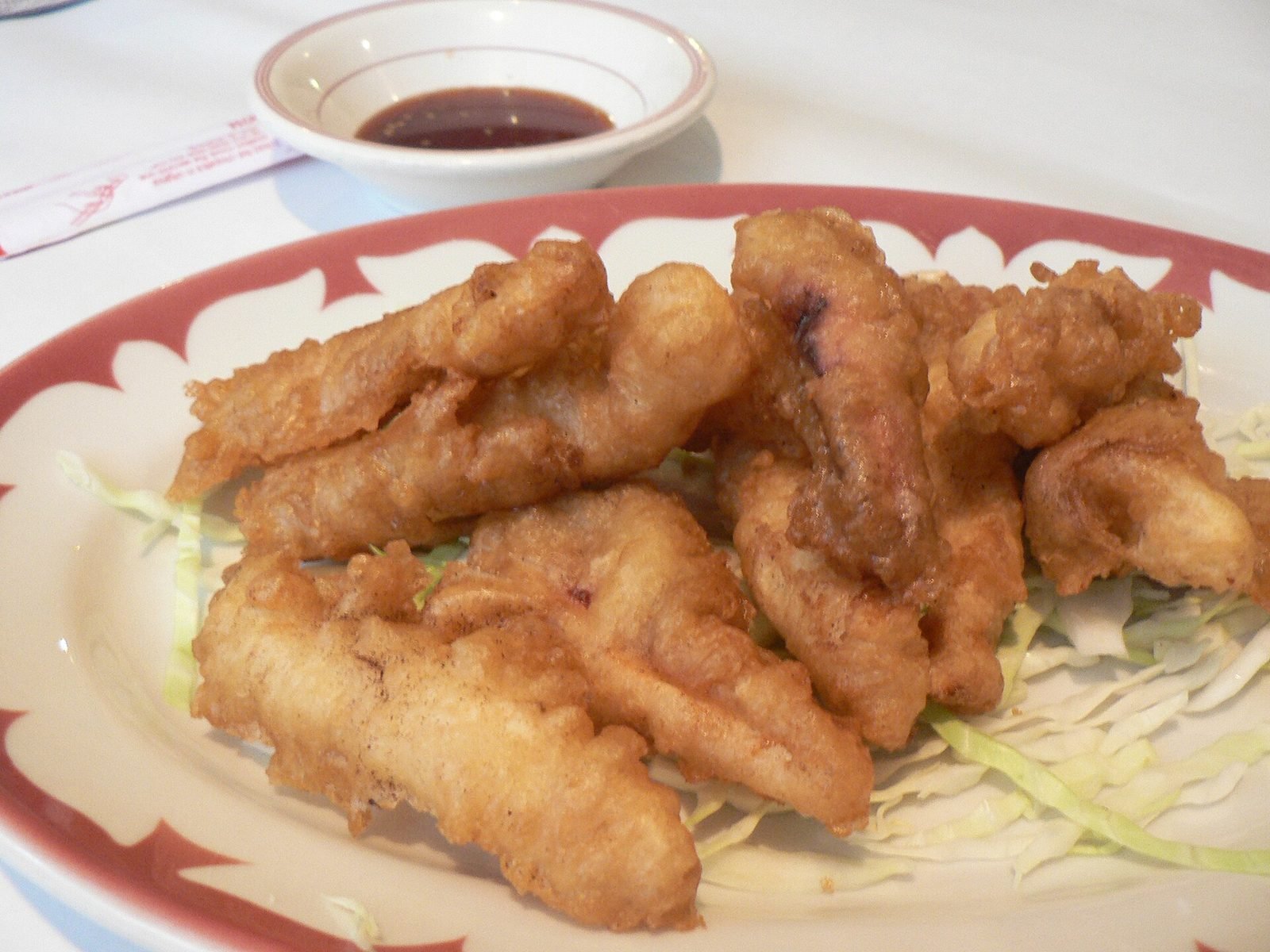 Plate of golden battered fried squid on shredded cabbage with a small dish of dark dipping sauce