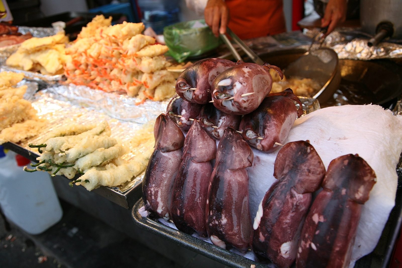 Street stall tray of battered fried vegetables next to skewered squid at a Korean port market