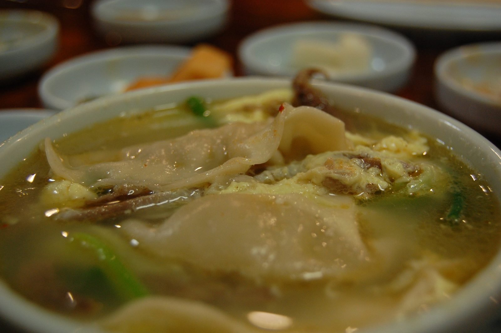 Close view of a bowl of mandu-guk with dumplings and egg in clear broth