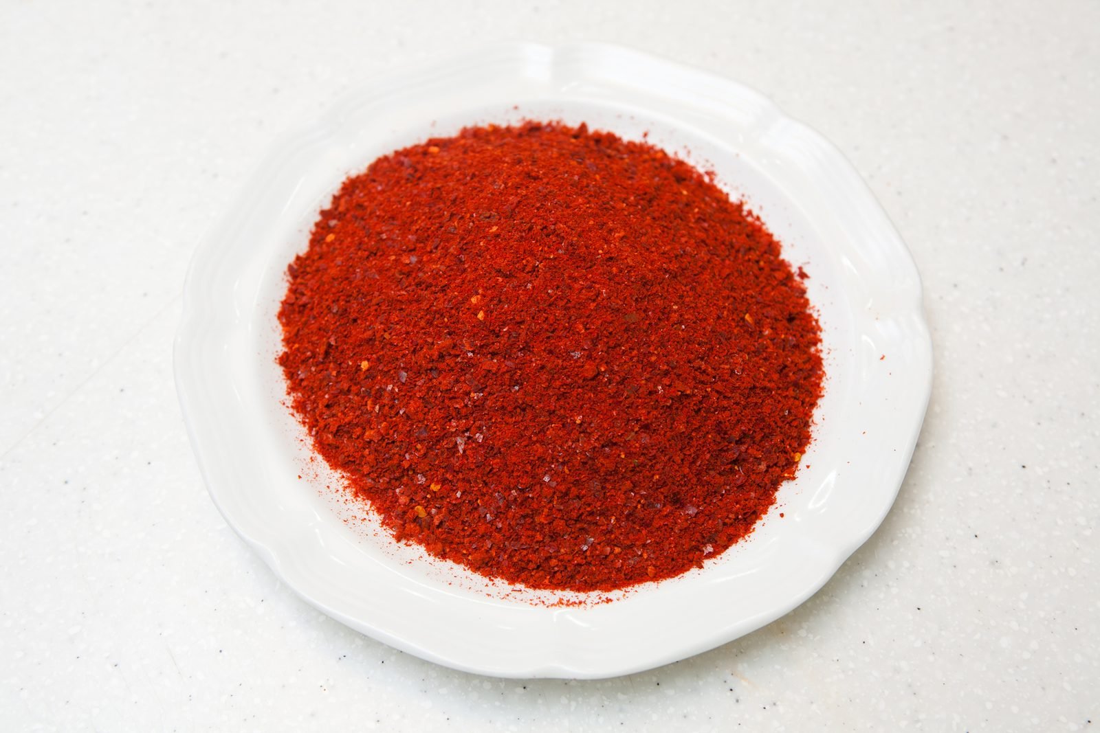 Pile of bright red coarse Korean chili flakes on a white plate