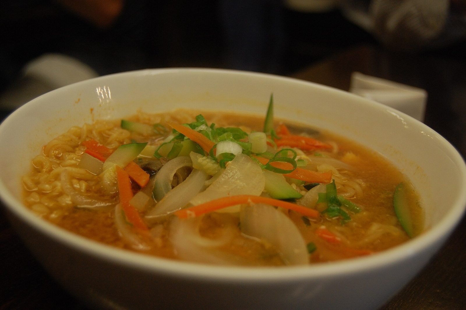 White bowl of Korean ramyeon with carrot, onion, zucchini and scallion floating in an orange broth