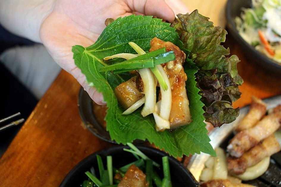 Hand holding a lettuce and perilla leaf wrap with grilled pork and sliced onion