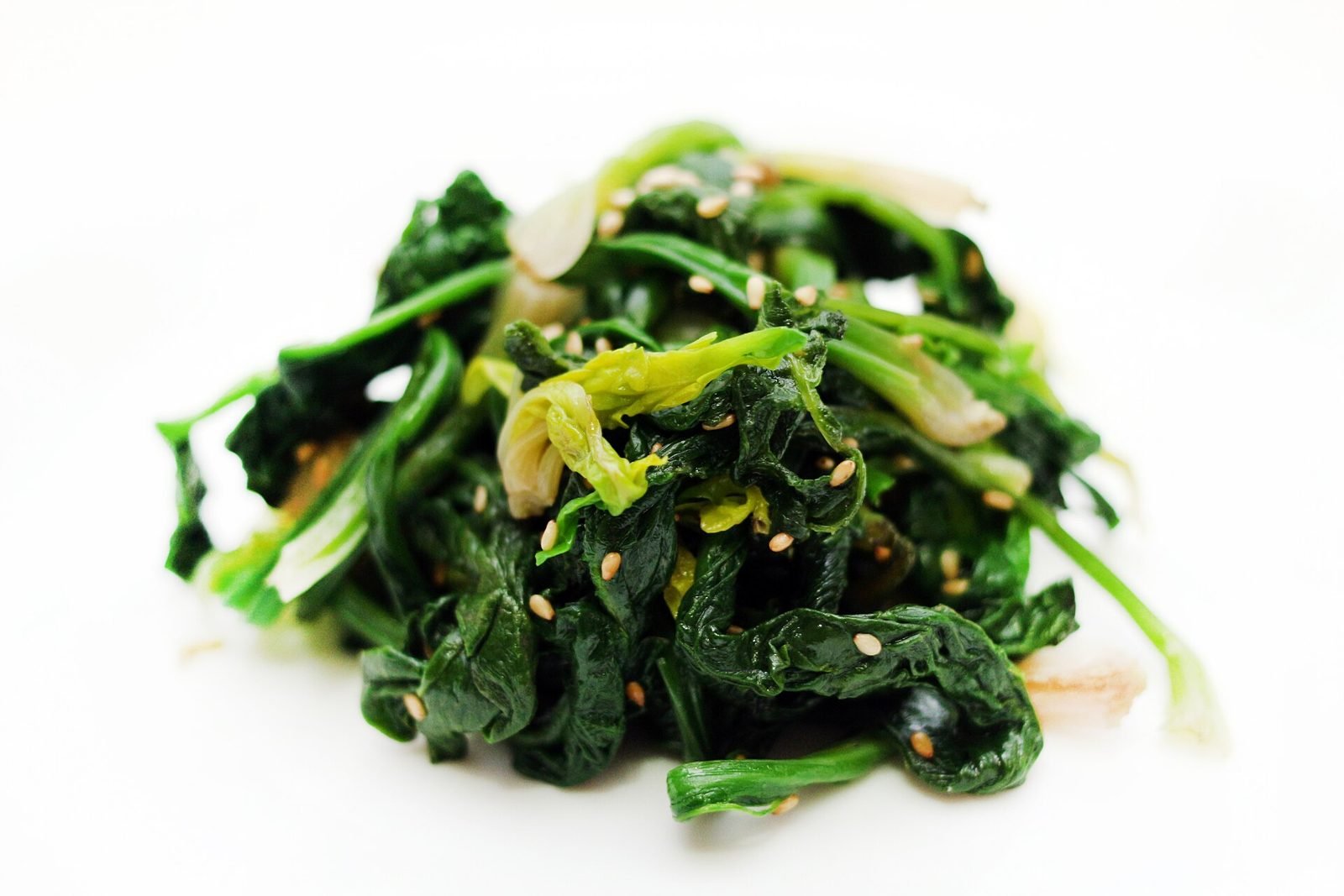 A small mound of seasoned dark green Korean spinach with sesame seeds on a white plate
