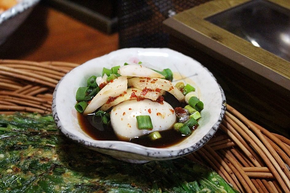 Dark soy dip with sliced scallions and chili in a white dish beside a pancake