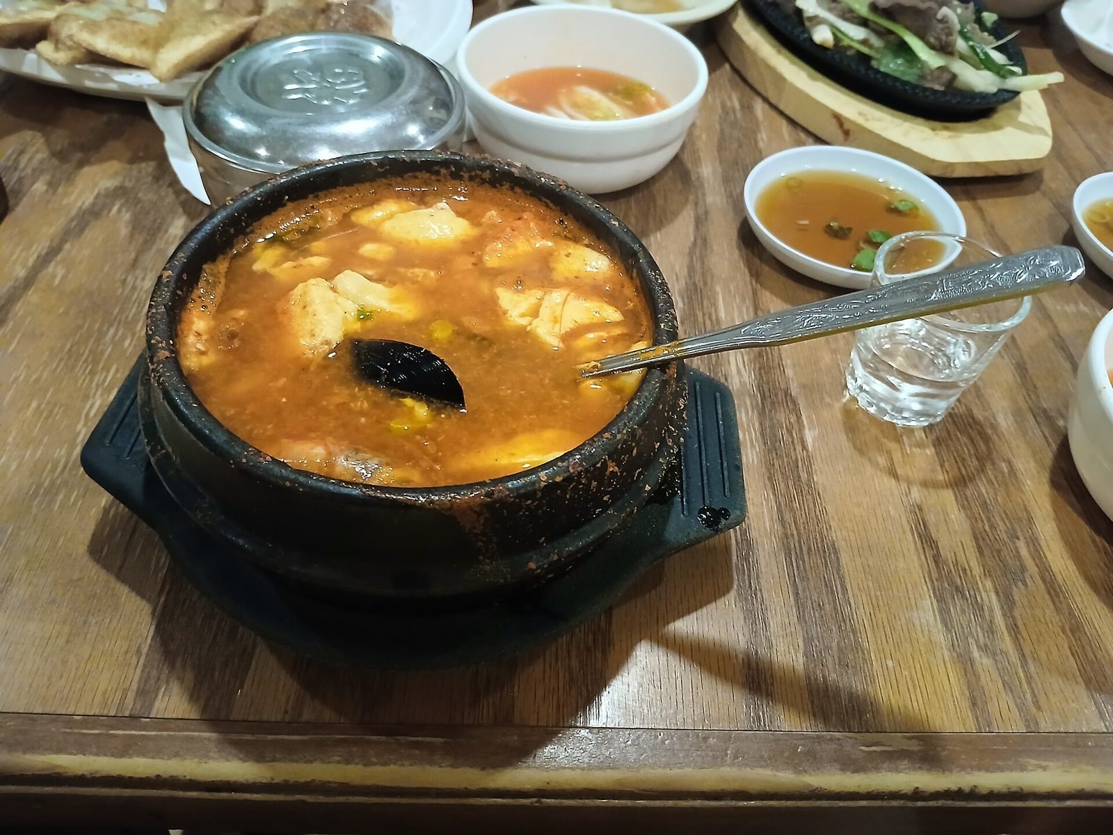 Bowl of sundubu jjigae with seafood, beef and a cooked egg in red broth