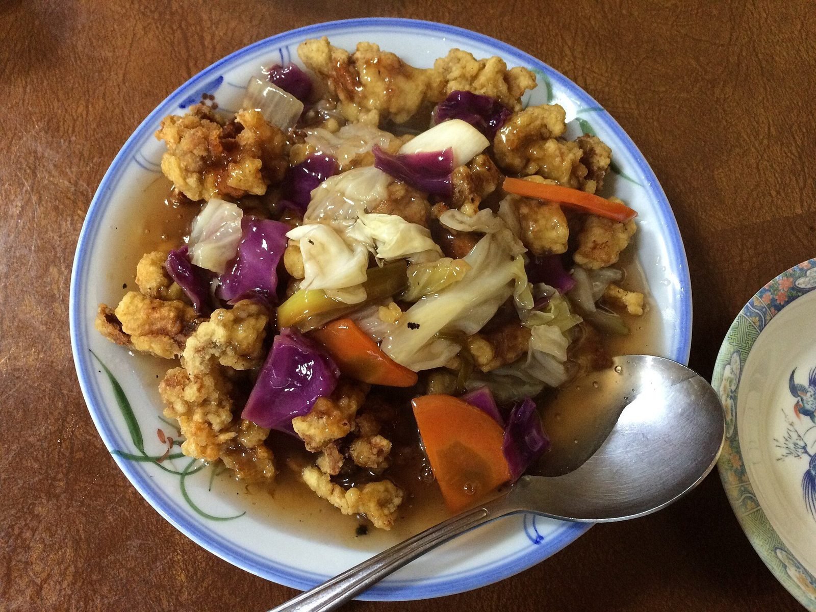Sweet and sour fried pork pieces with cabbage and carrot in a bowl with a spoon